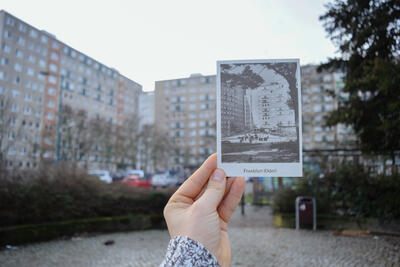 Bild vergrößern: Polaroid mit Silhouette vor Wohnblock gehalten.