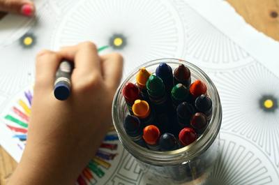 Bild vergrößern: Kinderhand, die mit Wachsmalstiften malt.
